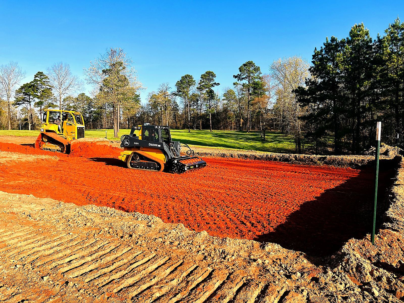 Skid steer grading a red clay pad